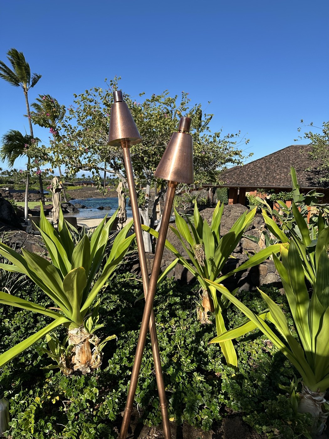 Close-up of a copper tiki torch with tropical garden backdrop